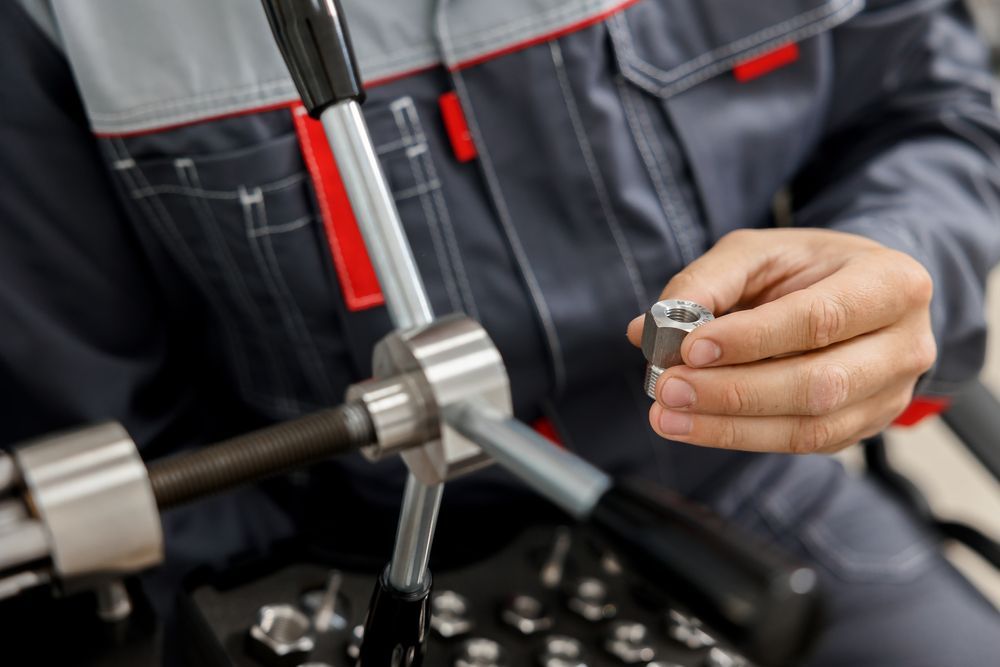 Mechanic in grey jumpsuit holds a metal nut, near a tapping tool.