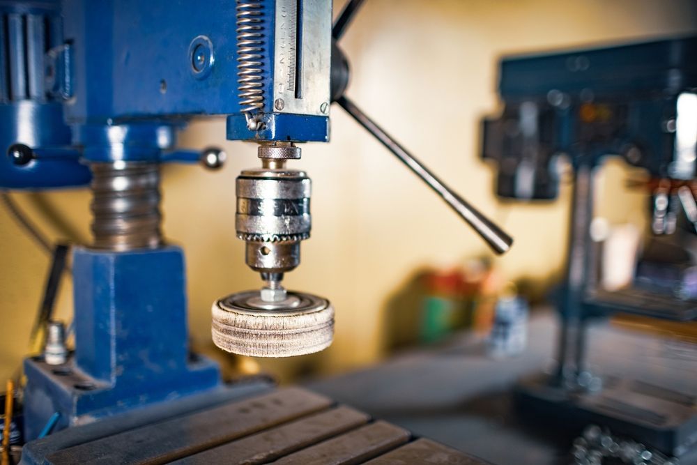 Blue drill press with attached buffing wheel, indoors.