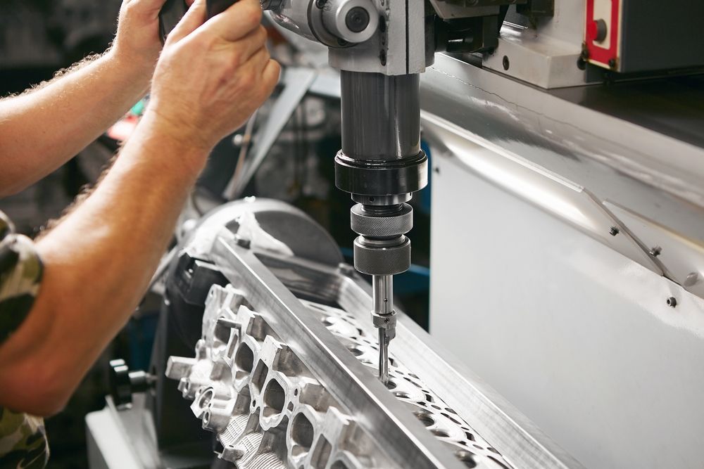 Person using a drill press to work on a metal object in a workshop setting.