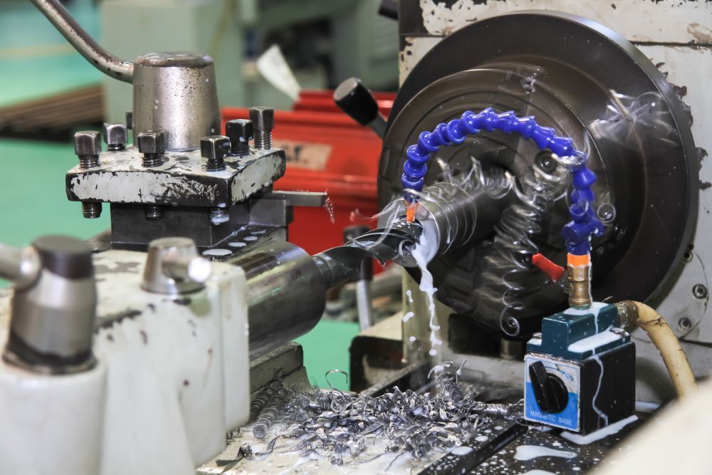 Lathe machine cutting metal, spraying coolant, surrounded by metal shavings.