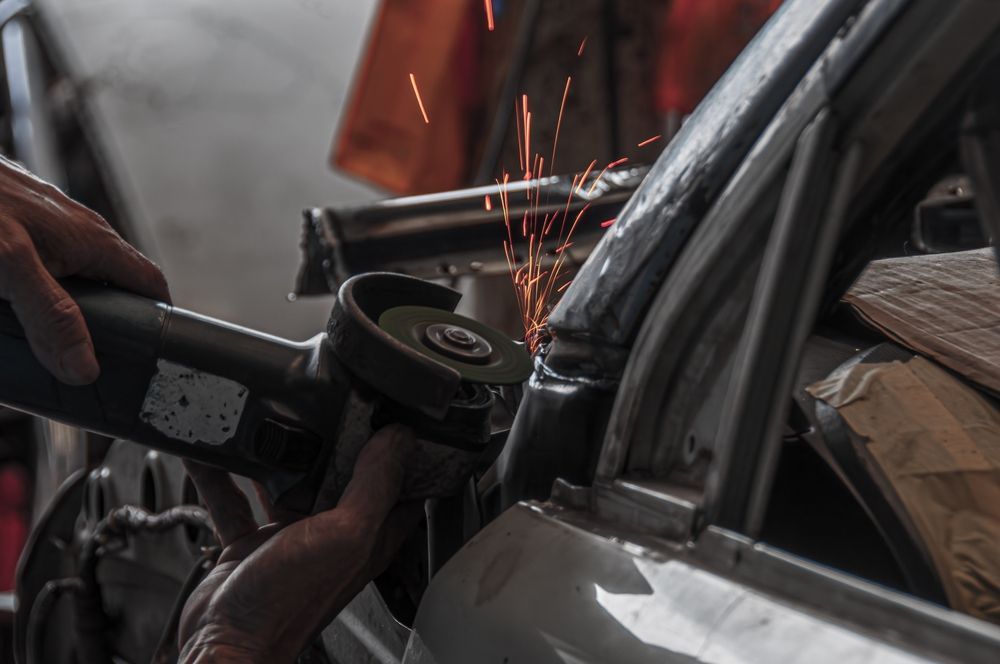 Person grinding metal on a car, sparks flying.