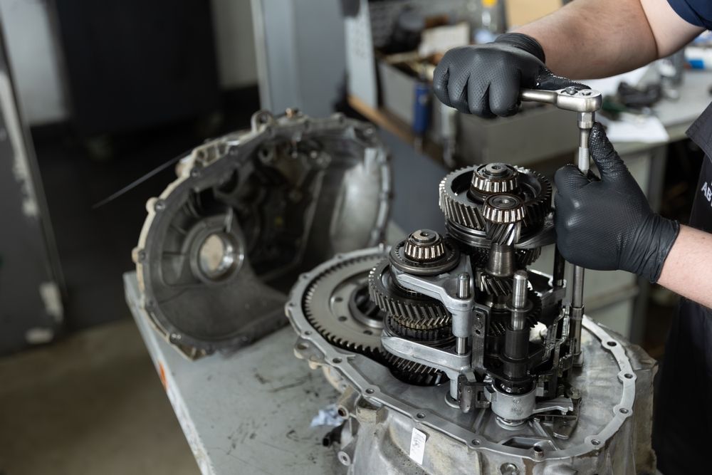 Mechanic with black gloves, using a wrench on a disassembled car transmission.
