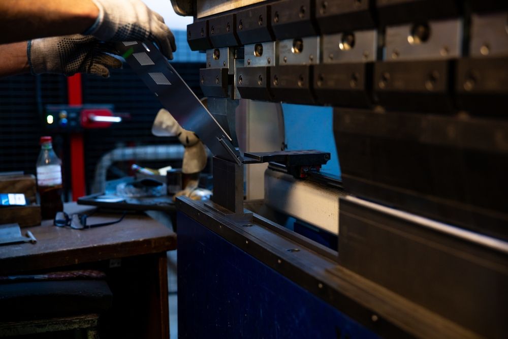 Person operating a metal bending machine in a workshop, bending a metal sheet.