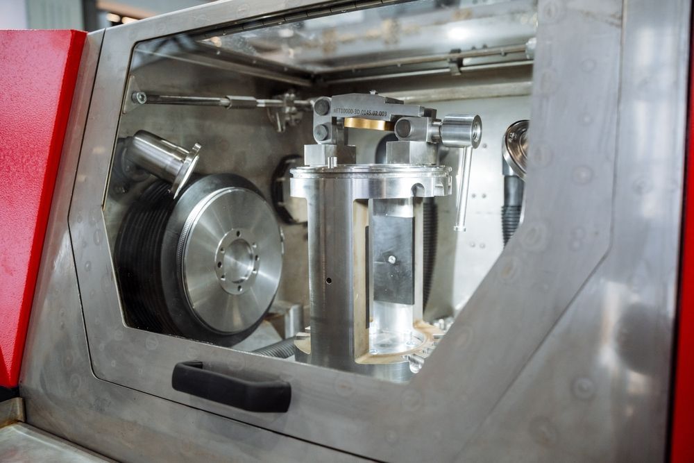 Inside a metal machine: cylindrical device with a black wheel, and other metal components. Red side panel is visible.