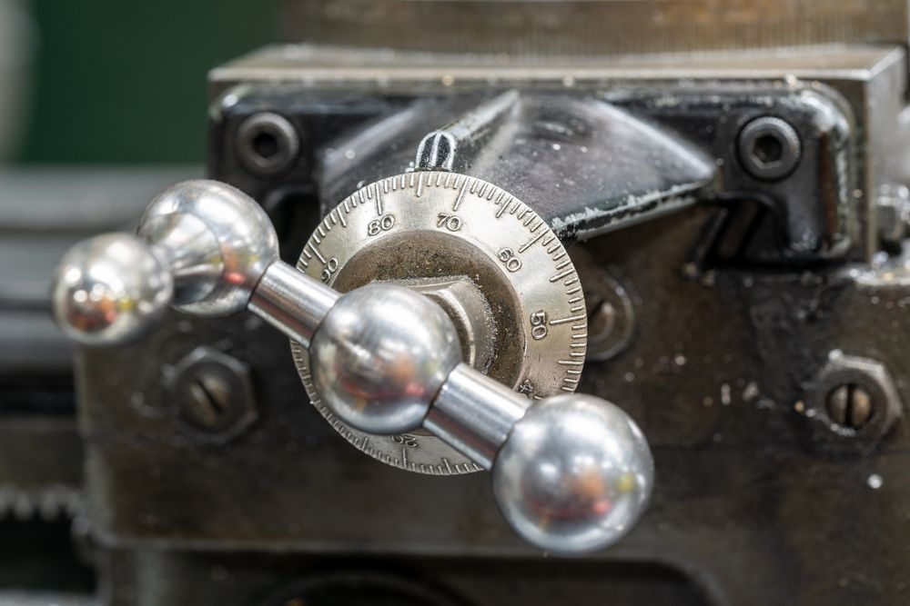 Close-up of a metal lathe handwheel with a numbered dial and silver handles.