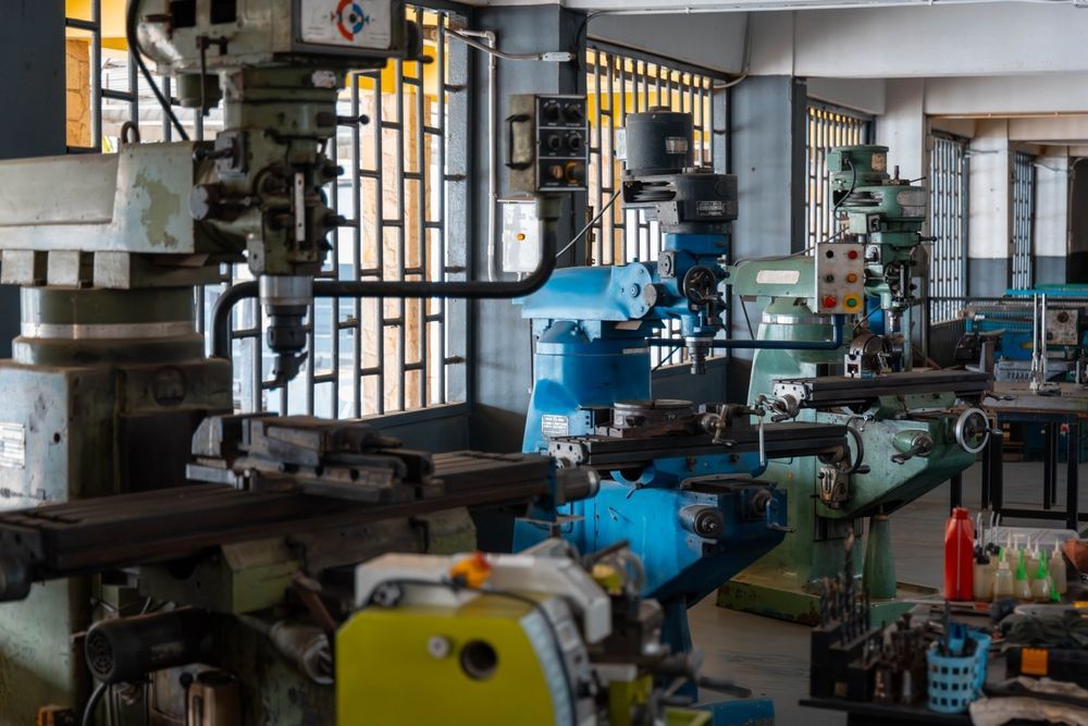Workshop with industrial machinery; milling and lathe machines near windows with barred light.