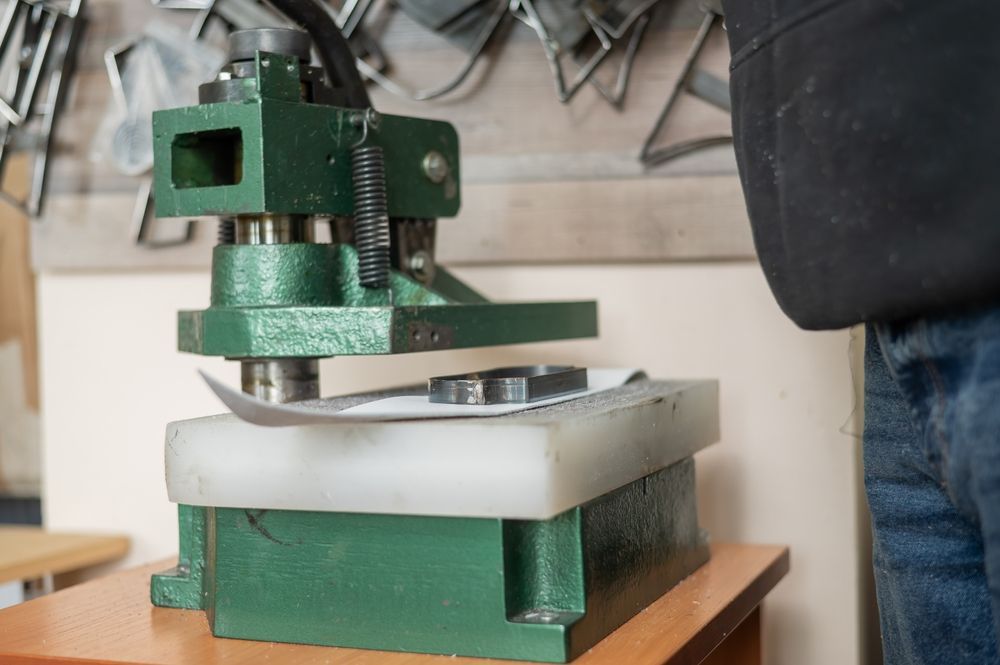 Green metal press tool stamping a small metal shape on a work surface.