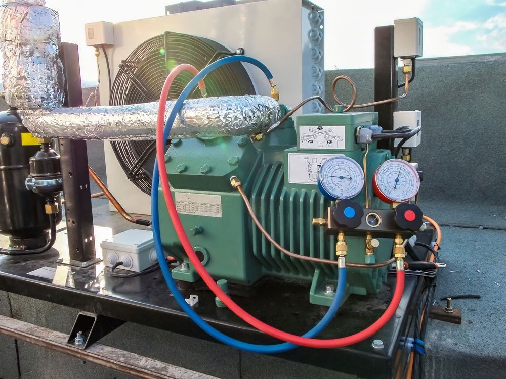 Green refrigeration compressor with gauges and hoses on a rooftop.