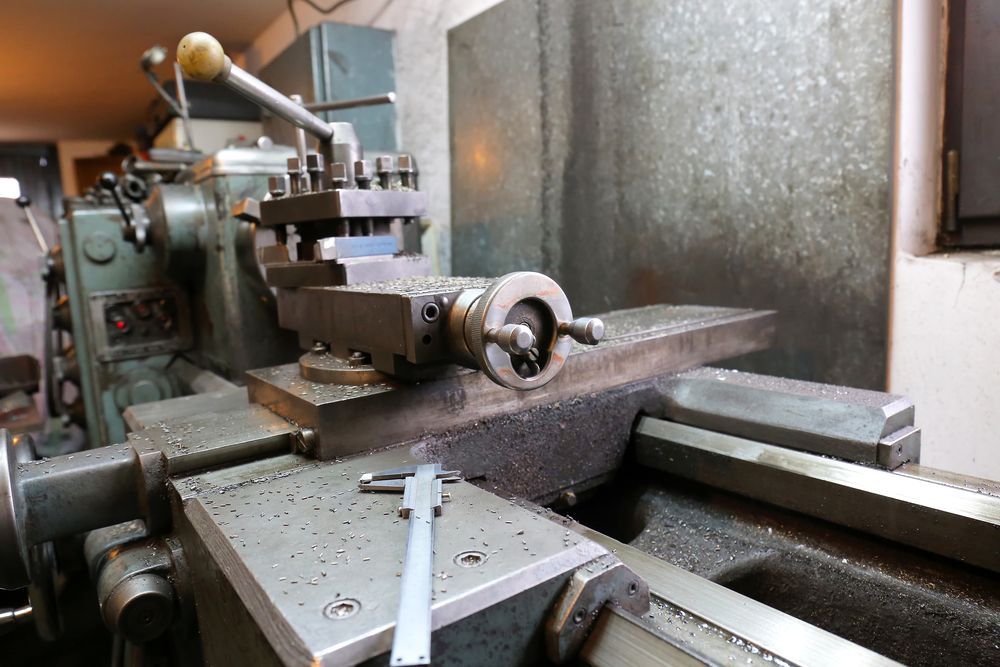A metal lathe machine with a caliper, covered in metal shavings, in an industrial setting.