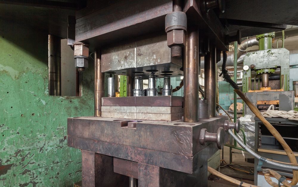 Heavy industrial press with a mold. Green walls and equipment in background.