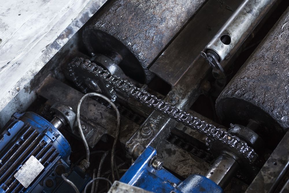 Industrial machinery with a chain drive system, blue motors, and greasy components.