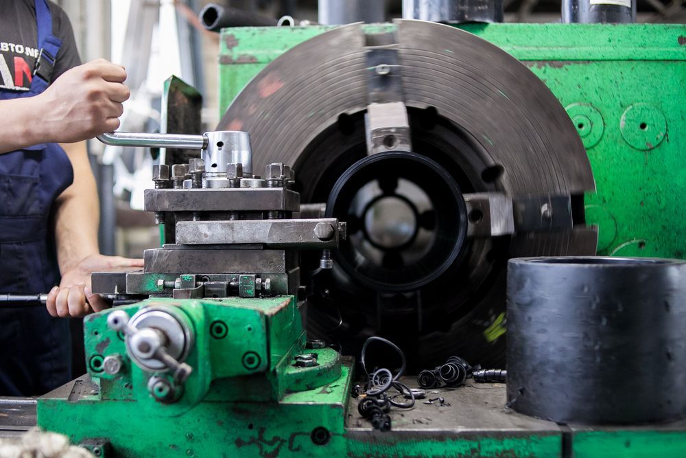 Green metal lathe in a workshop, used by a person to shape a metal piece.