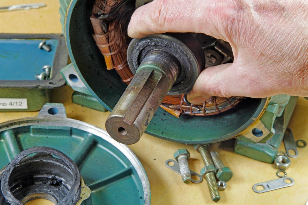 Hand holding motor shaft, exposing internal copper wiring and green metal housing.