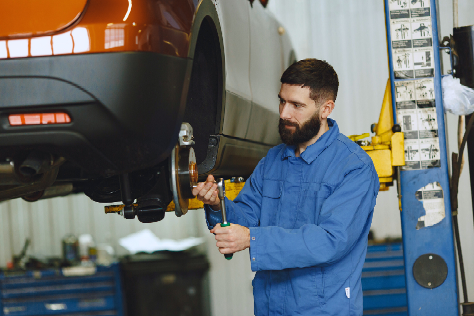 Mechanic in blue coveralls using a wrench on a car wheel assembly in a garage.