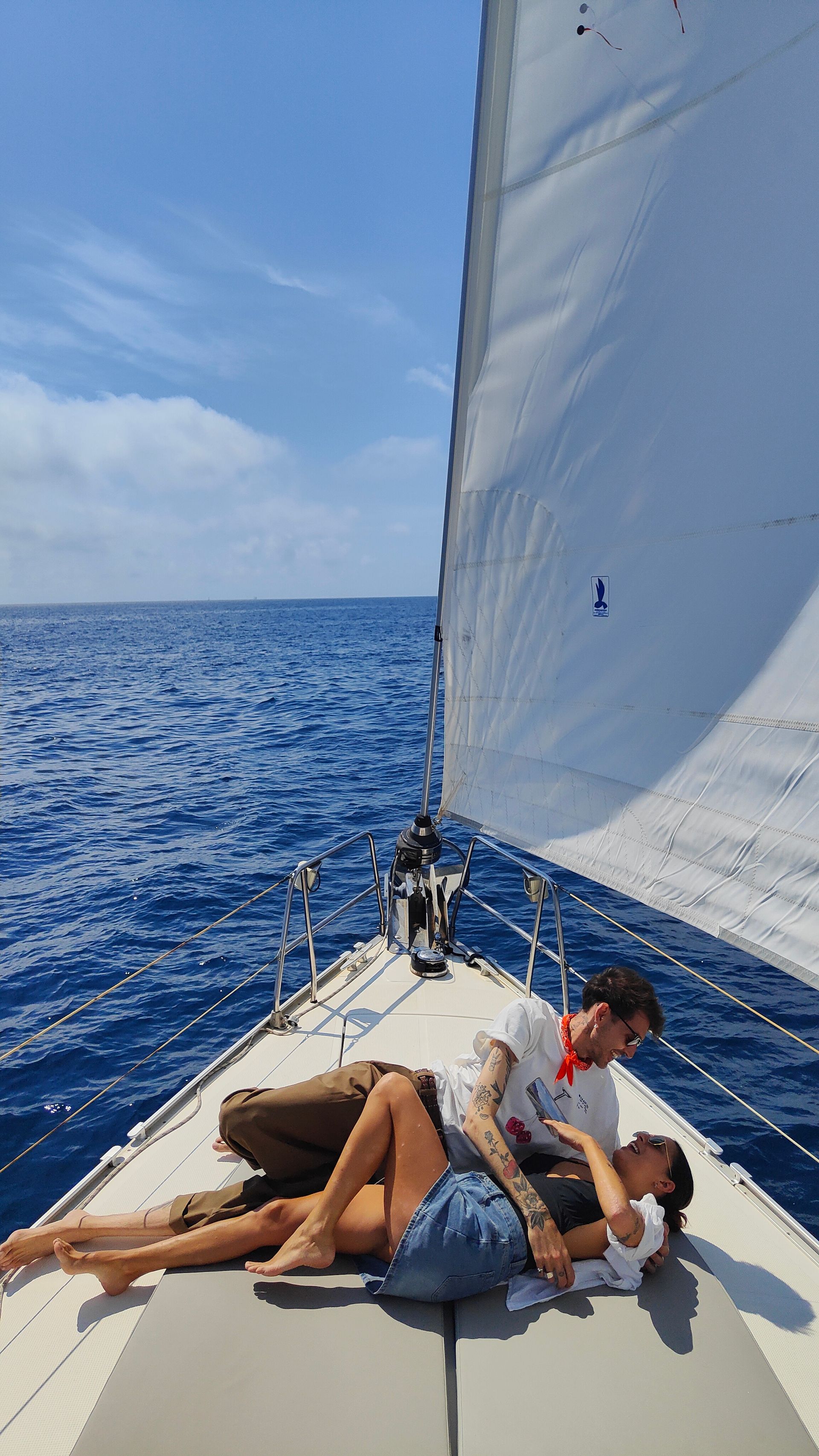 Un hombre y una mujer están acostados en la parte trasera de un velero en el océano.