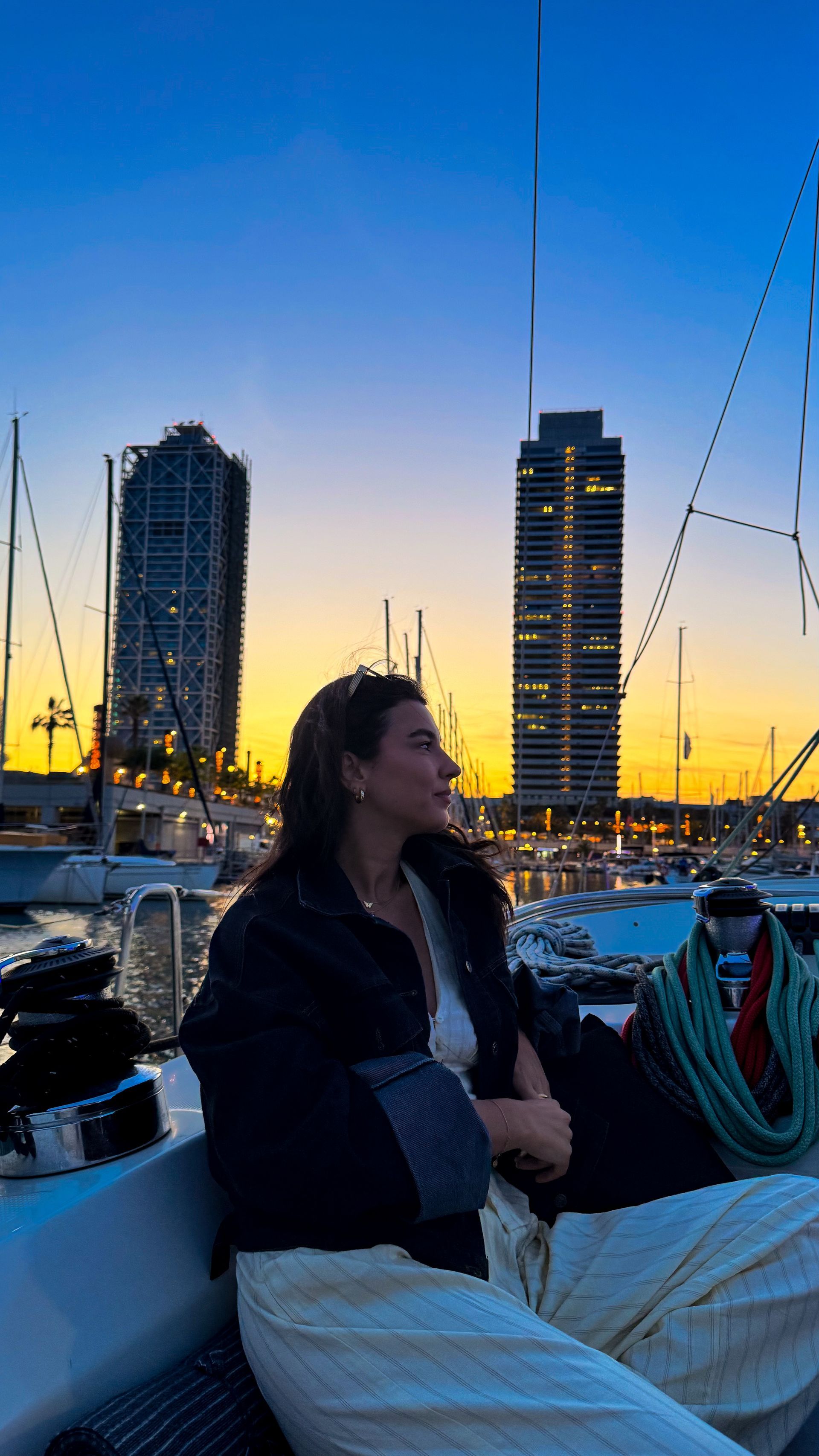 Una mujer está sentada en un barco frente al horizonte de una ciudad al atardecer.