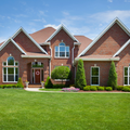 Brick suburban house with manicured green lawn and blue sky