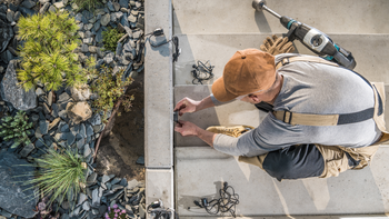 Worker using power tools to install pavers beside a landscaped gravel bed