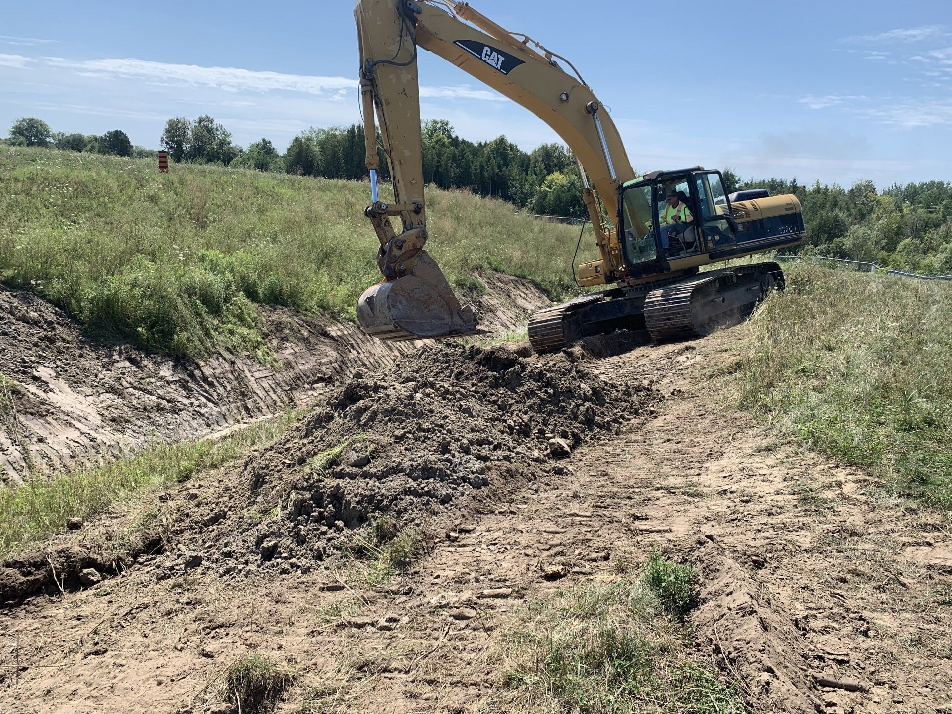 A large yellow excavator is digging a hole in a field.