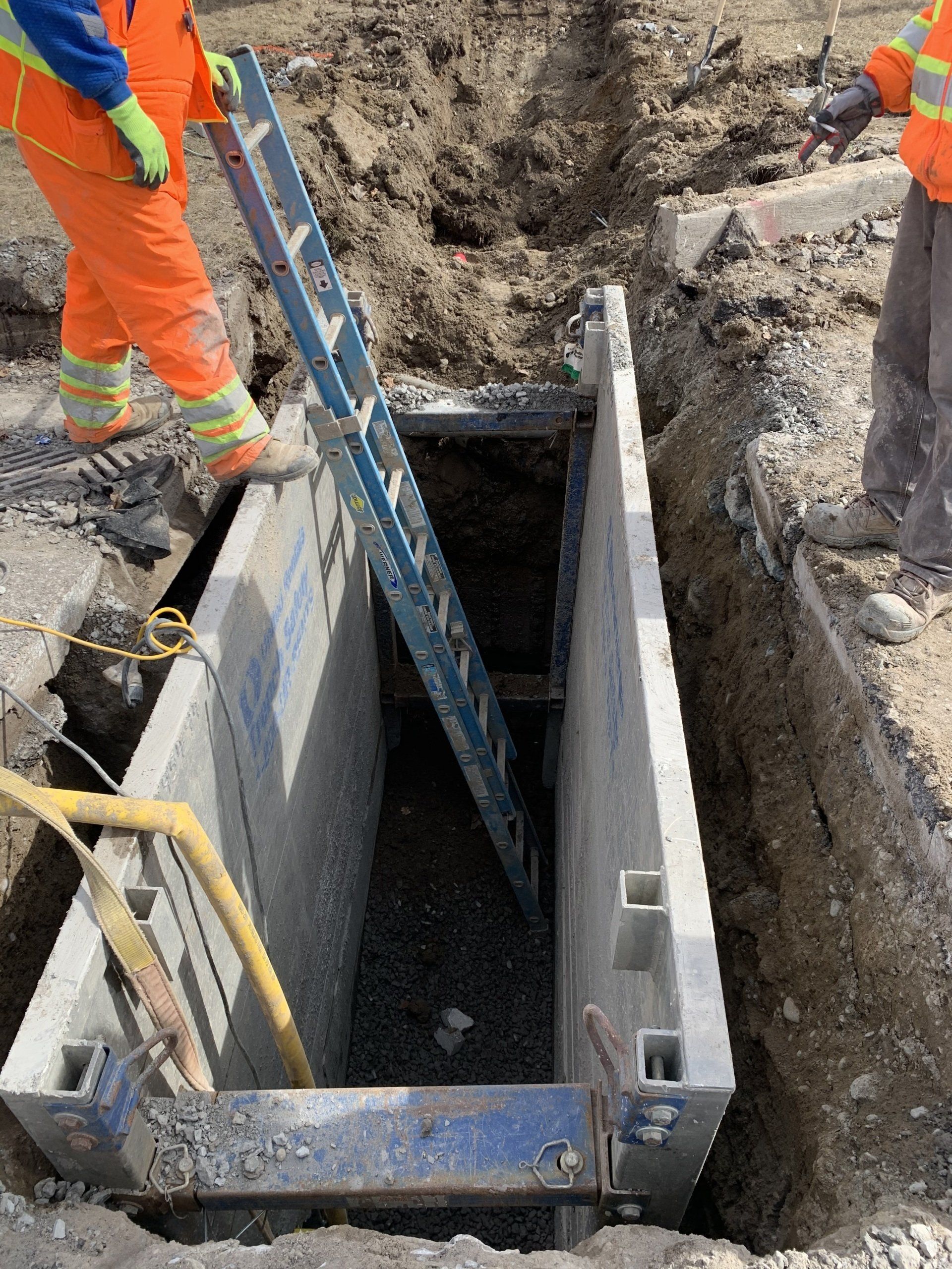 A man is holding a ladder in a hole in the ground.