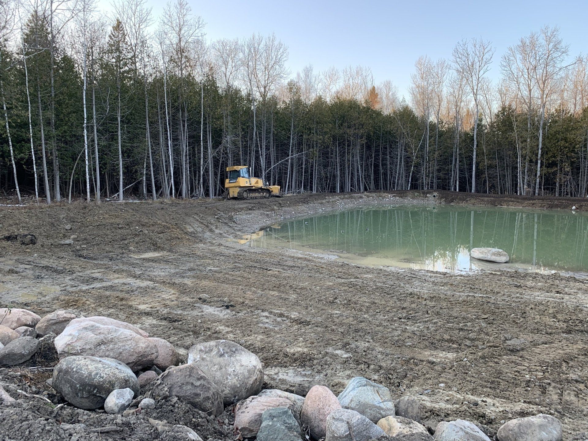A bulldozer is working on a pond in the middle of a forest.