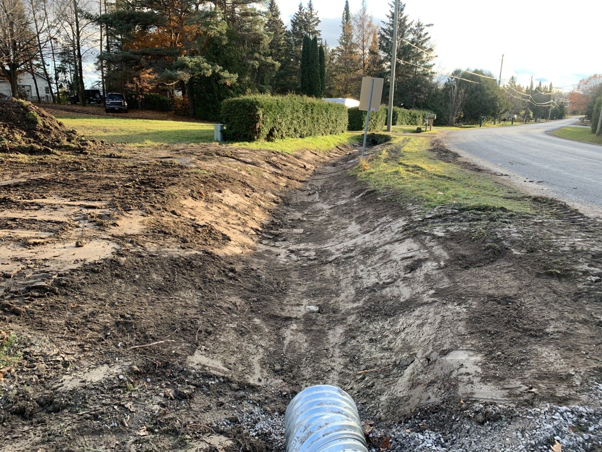 A large pipe is sitting in the middle of a dirt field next to a road.