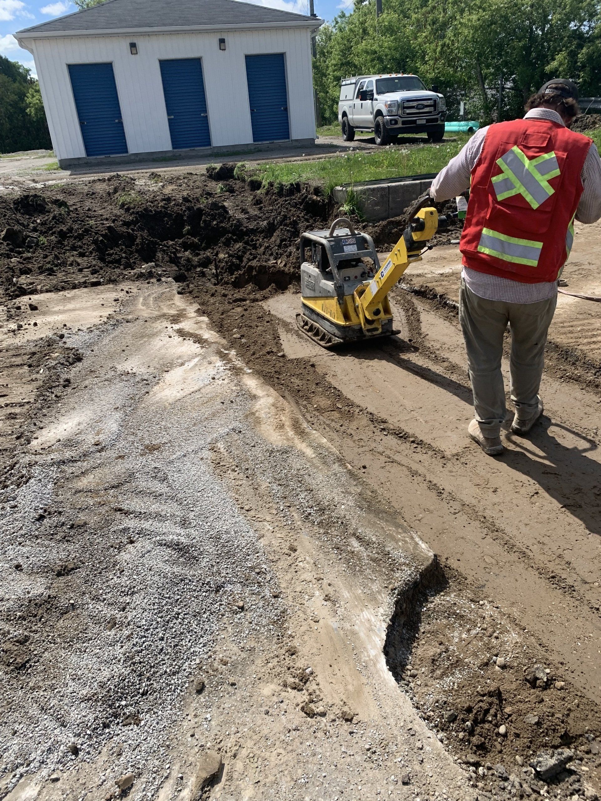 A man in a red vest is using a machine to level a dirt road.