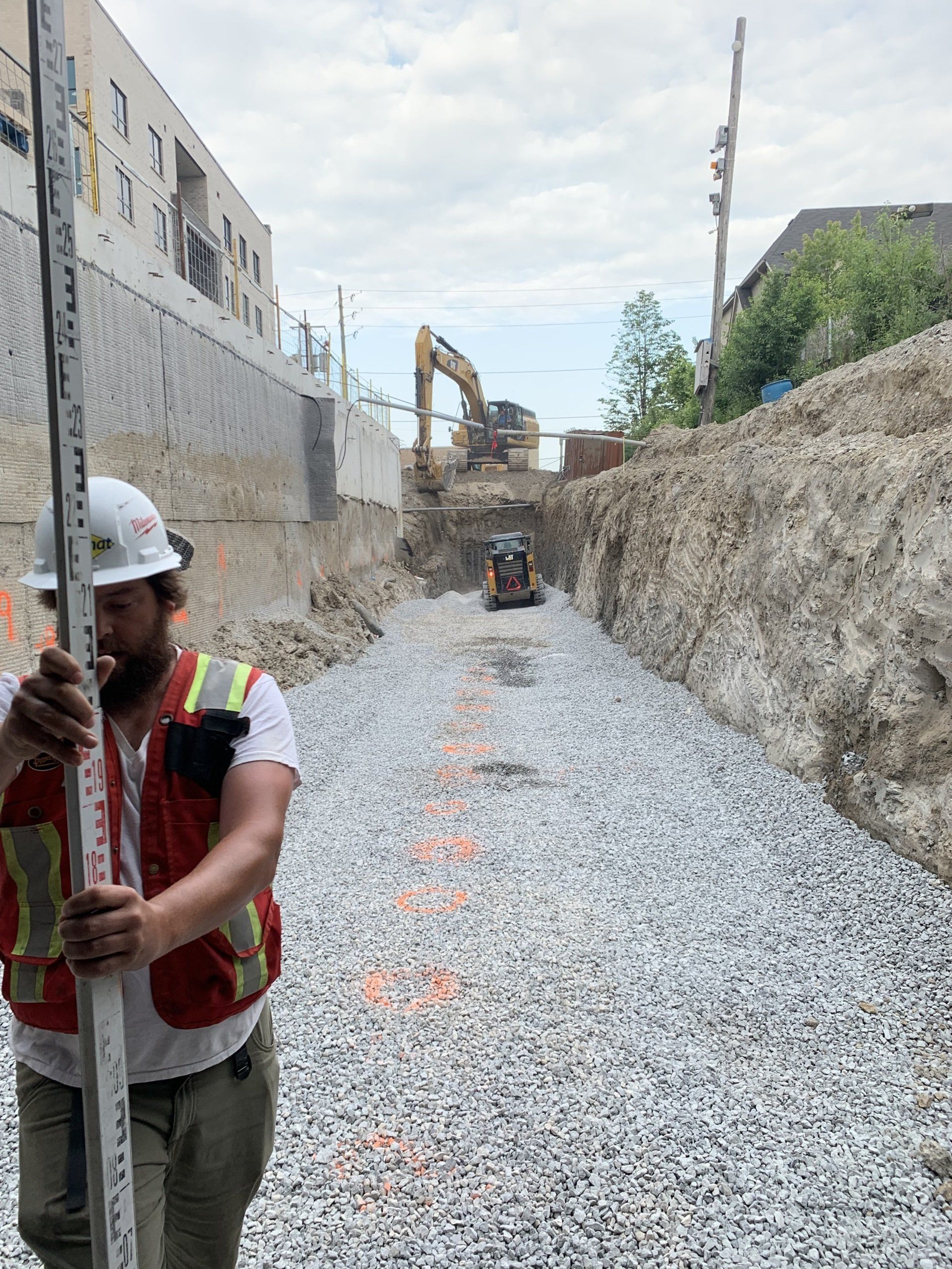 A construction worker is standing in a gravel area holding a level.