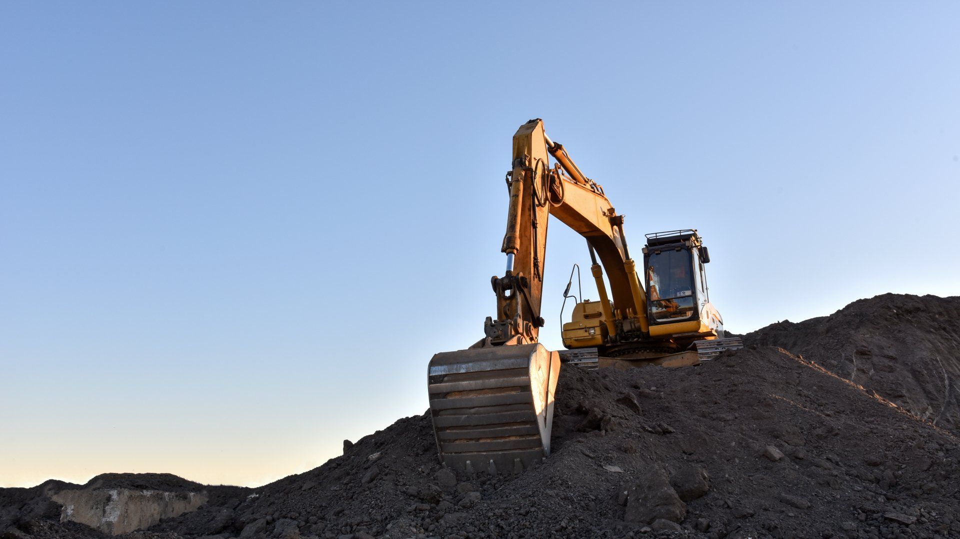 A yellow excavator is sitting on top of a pile of dirt.