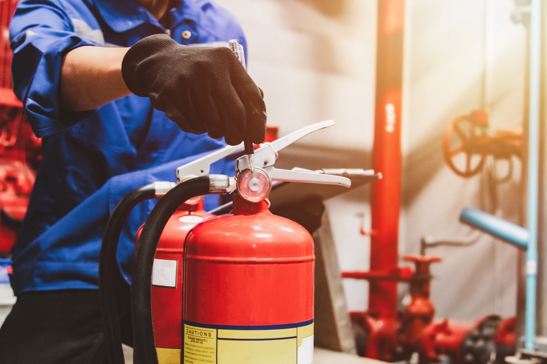 Gloved hand inspecting a fire extinguisher in an equipment room.