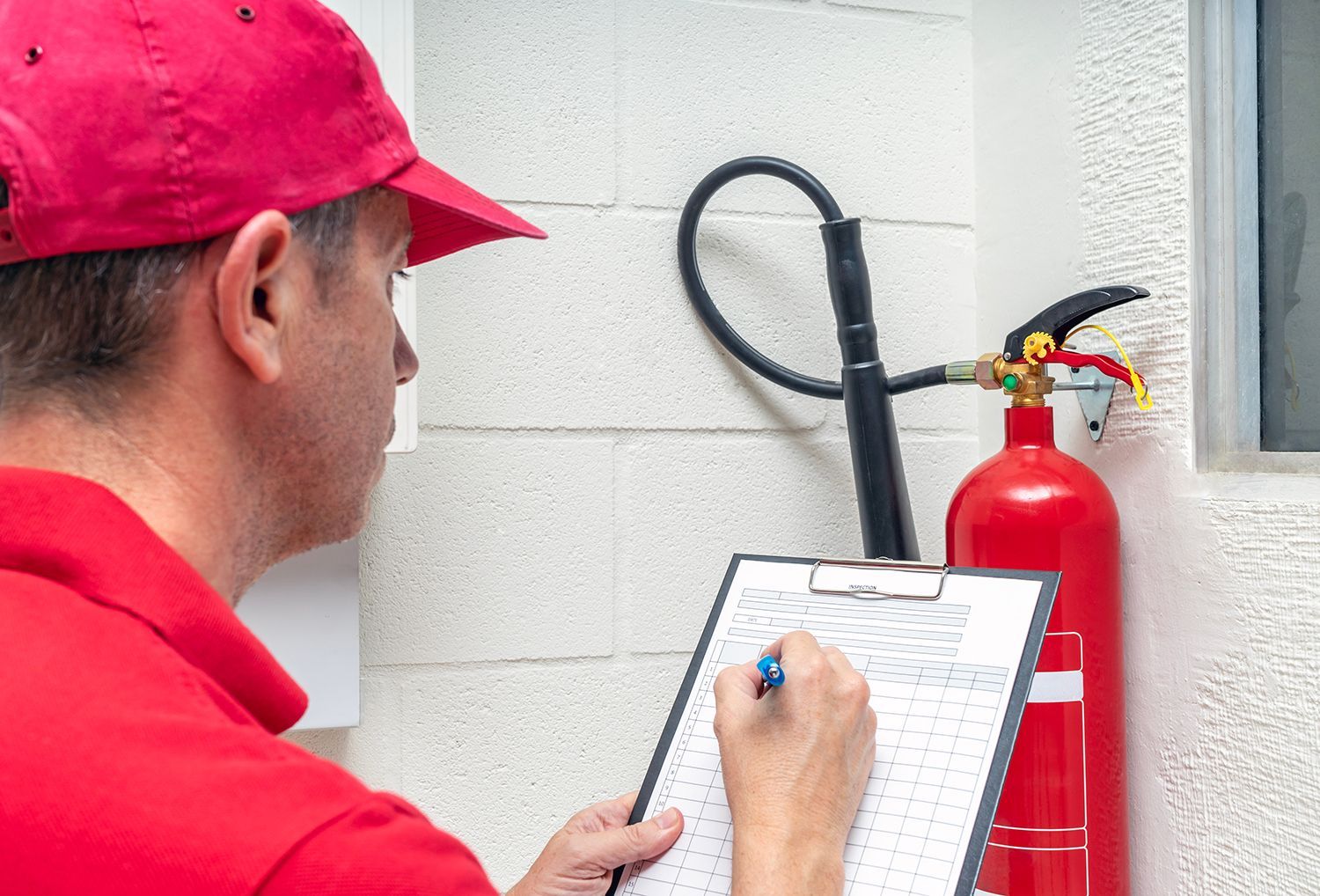 Technician inspecting a fire extinguisher and recording details on a safety checklist.