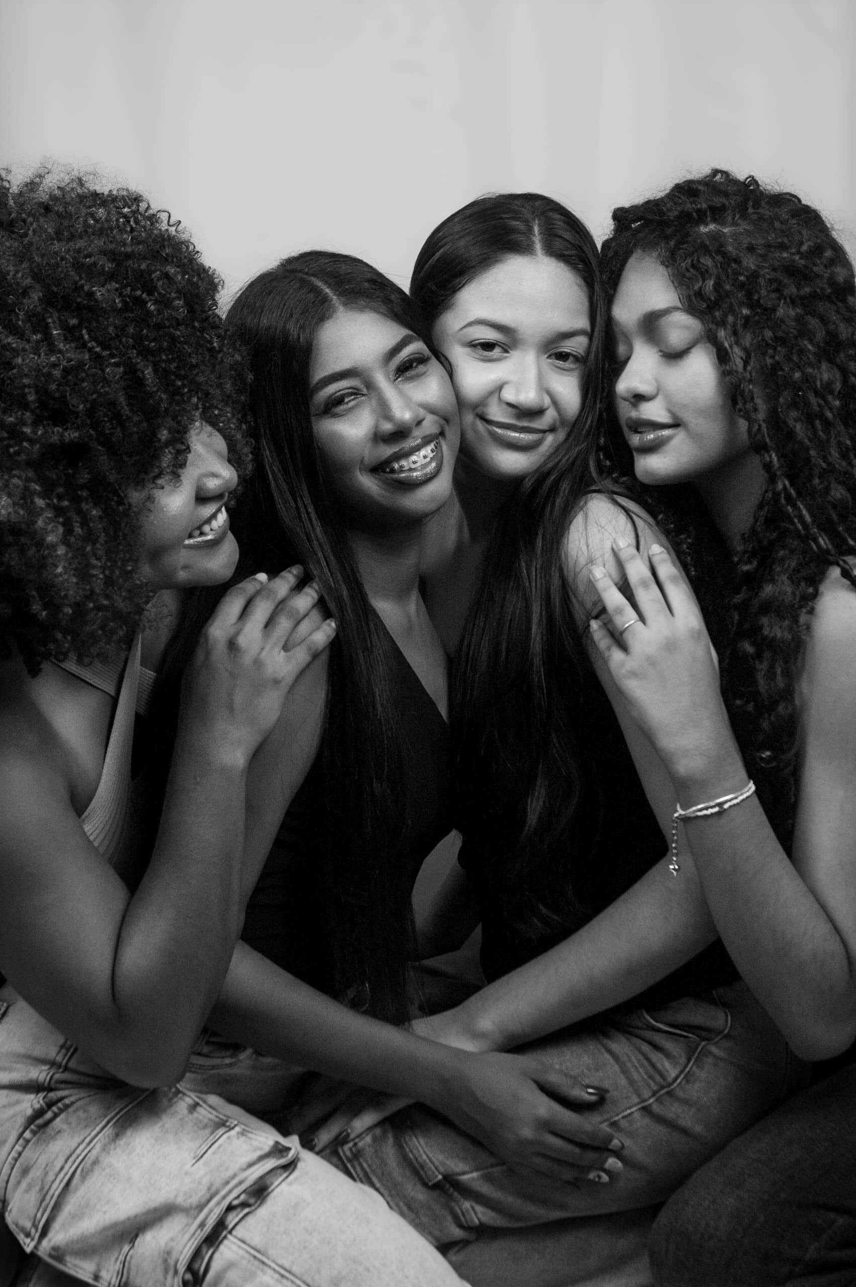 Four women embracing, smiling. Black and white photo; close-up.
