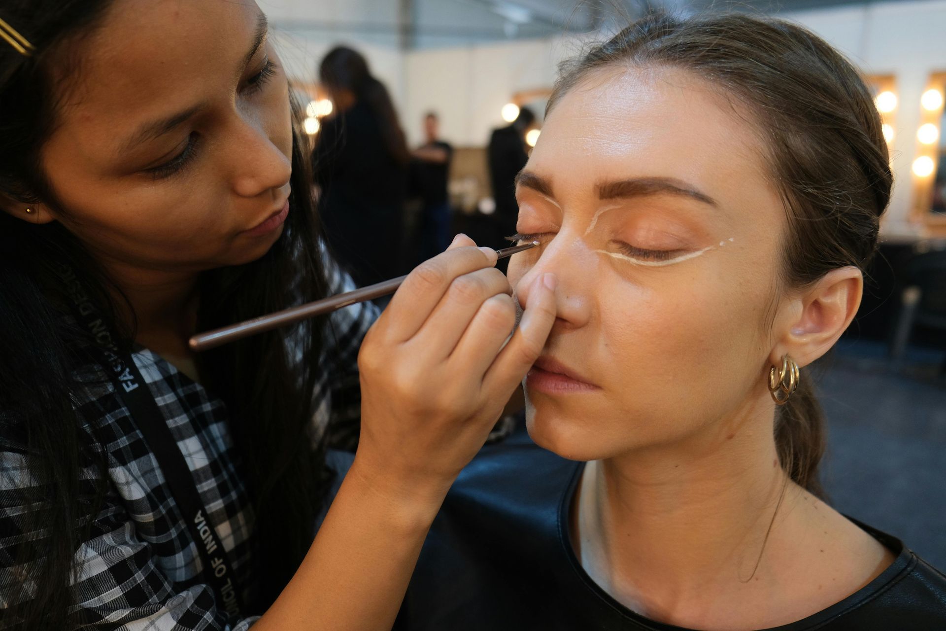 Makeup artist applying eyeliner on a model's face in a studio setting.