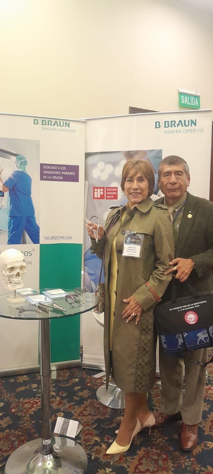 Una pareja se encuentra en un stand de una feria comercial, sosteniendo un instrumento médico y un maletín.