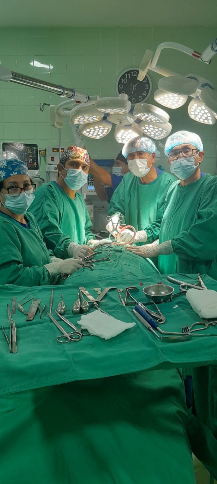 Equipo médico en quirófano, realizando una cirugía. Instrumental quirúrgico sobre tela verde. Luces brillantes en el techo.