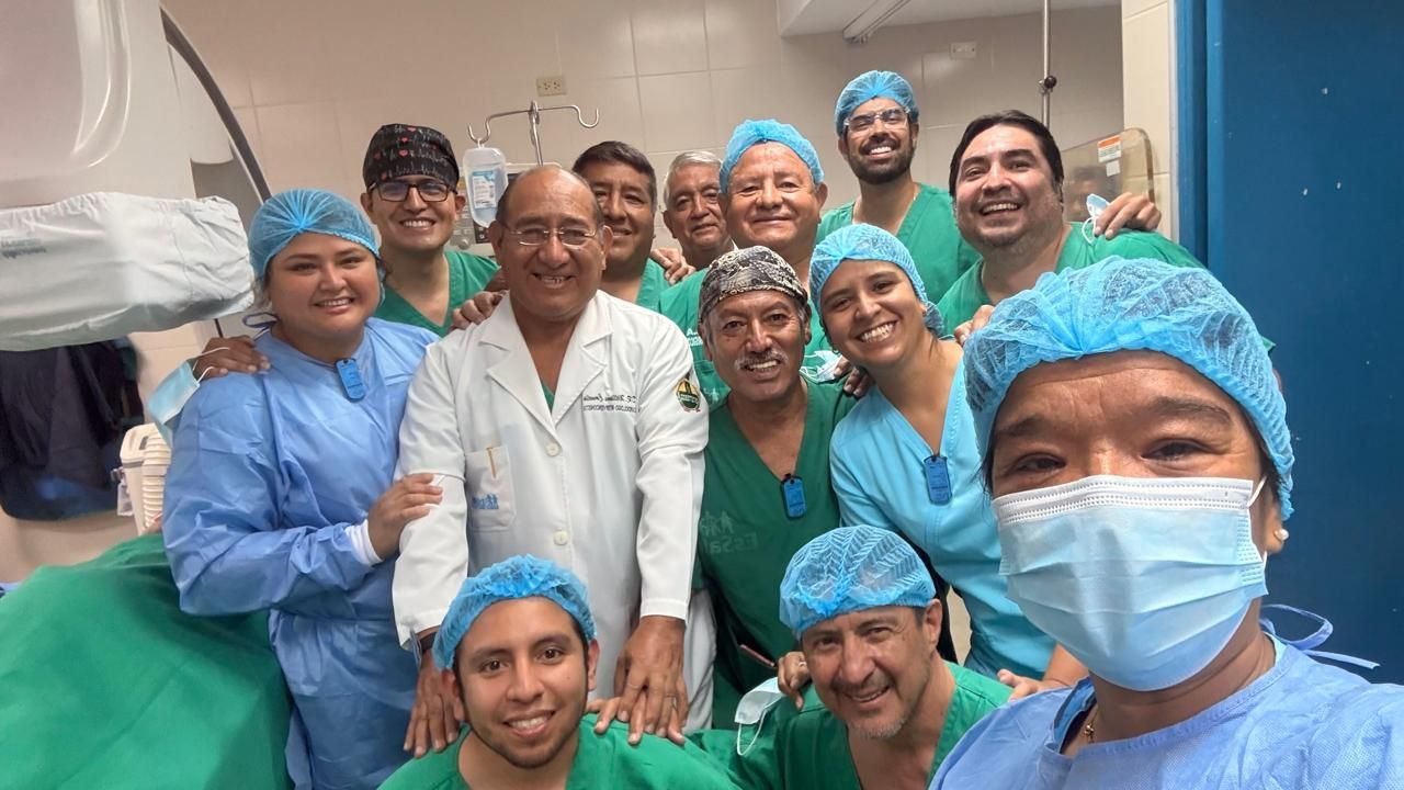 Equipo médico con uniformes y cofias, posando juntos en un quirófano.