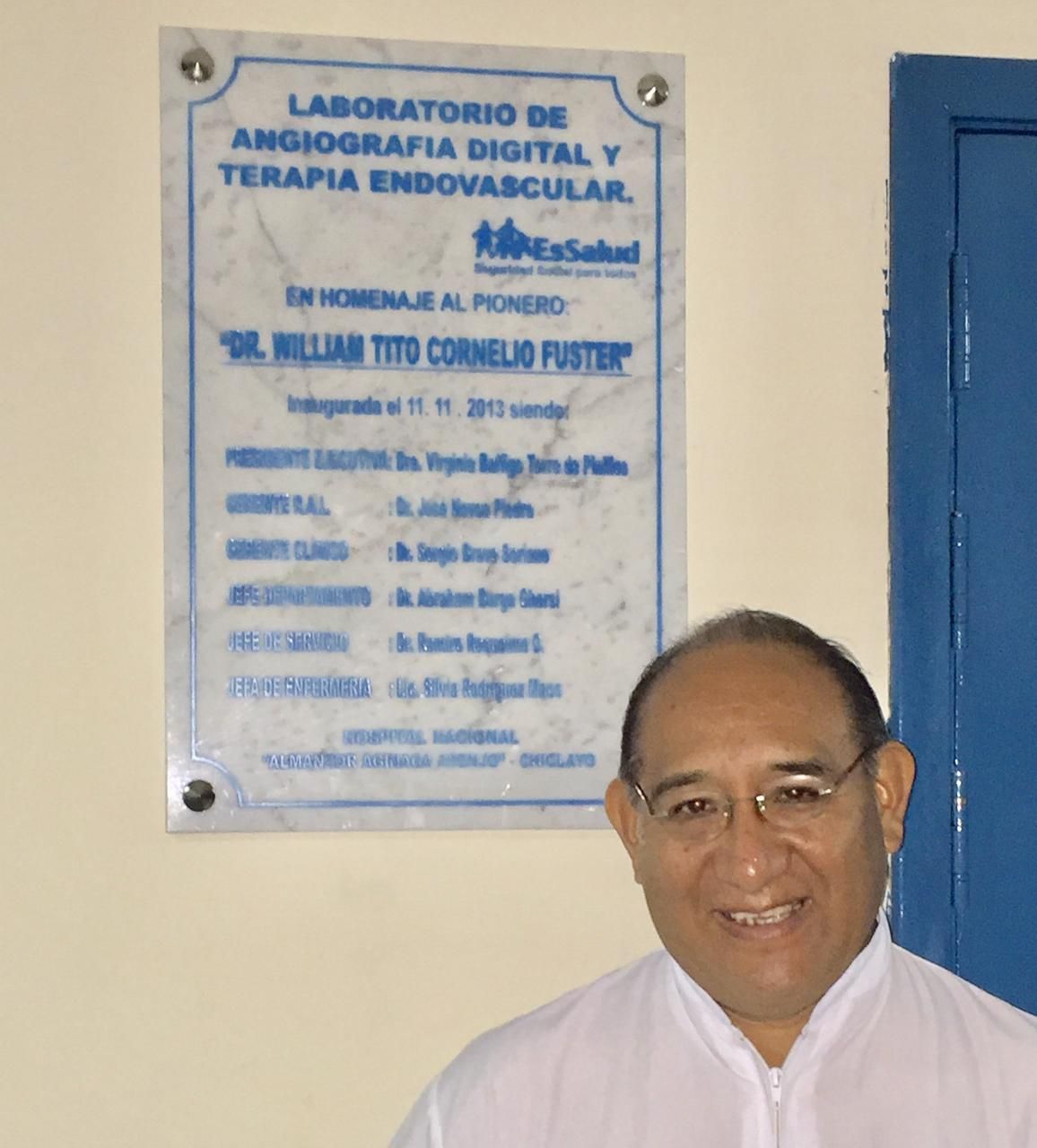 Hombre sonríe junto a una placa en honor al Dr. Millian Tito Cornelio Fuster