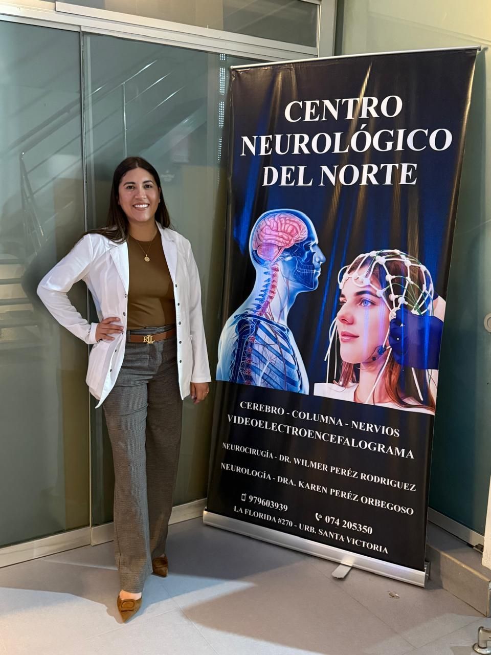 Una mujer con una chaqueta blanca está junto a una pancarta de un centro neurológico con ilustraciones del cerebro.