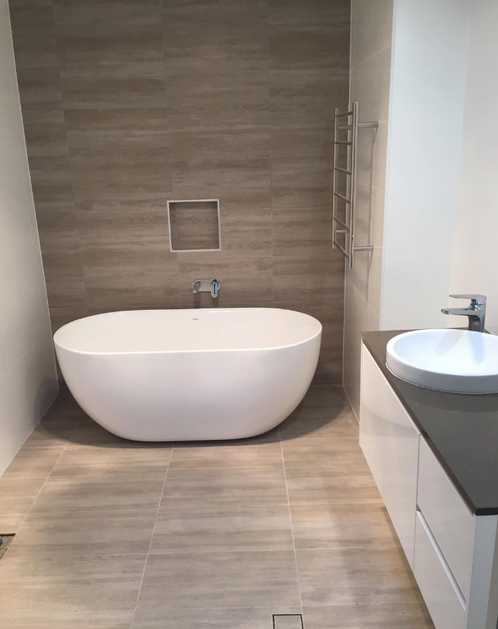 A White bathtub with light brown tiles and a towel holder — Seeto Tiling in Fingal Bay, NSW