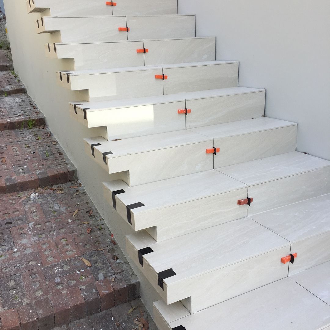 White Tile Steps Under Construction With Orange Levelers and Black Corner Pieces — Seeto Tiling in Medowie, NSW