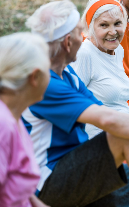Tre persone in abbigliamento sportivo sedute a chiacchierare all'aperto, con un'attenzione particolare su una persona sorridente che indossa una fascia arancione.