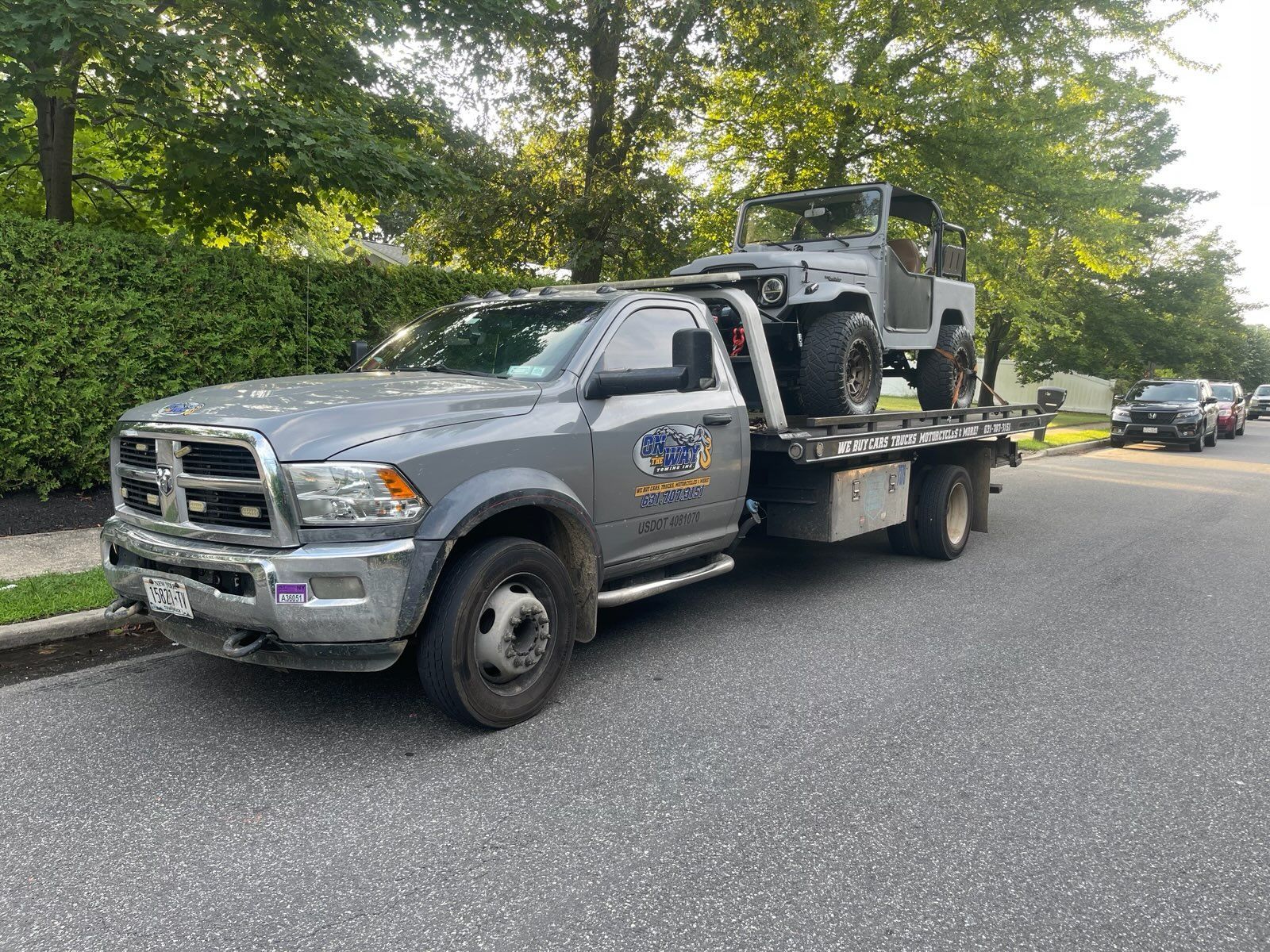 Gray tow truck carrying a gray Jeep on a residential street.