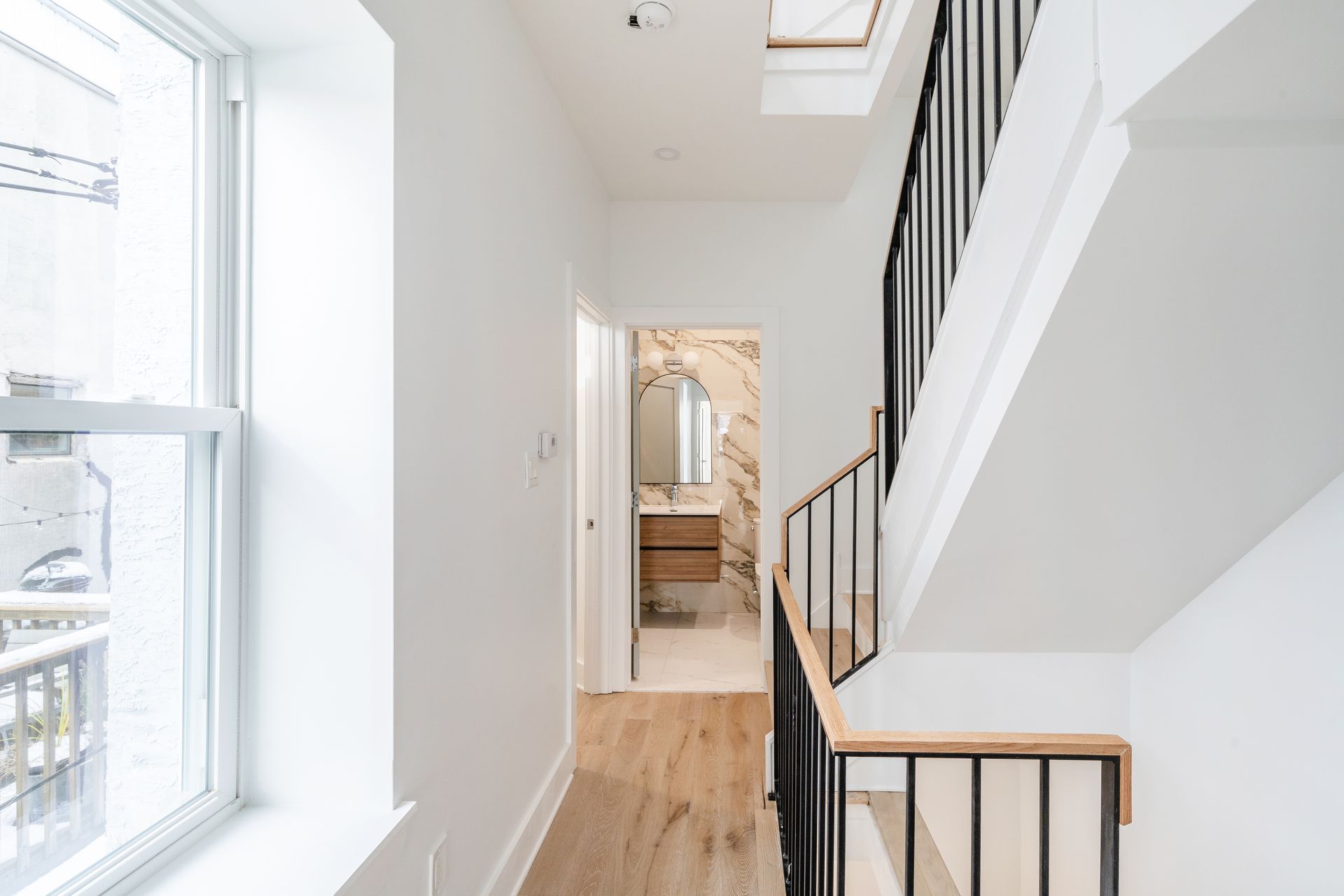 A hallway with stairs leading up to a bathroom and a window.