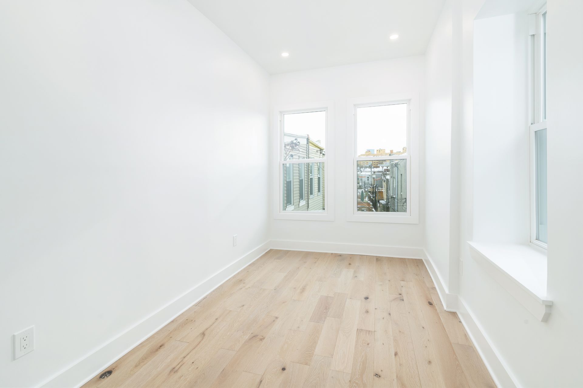An empty room with hardwood floors and three windows.