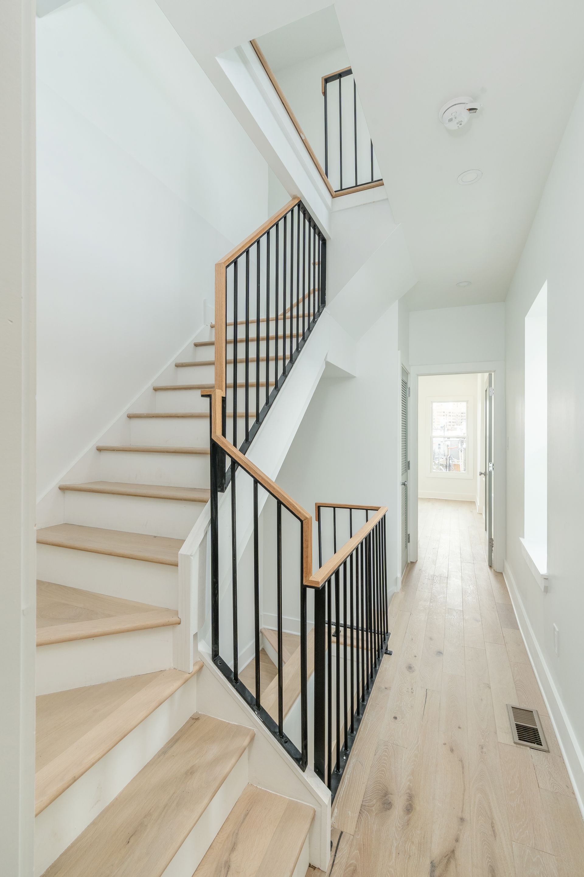 A staircase with wooden steps and a black railing in a hallway.