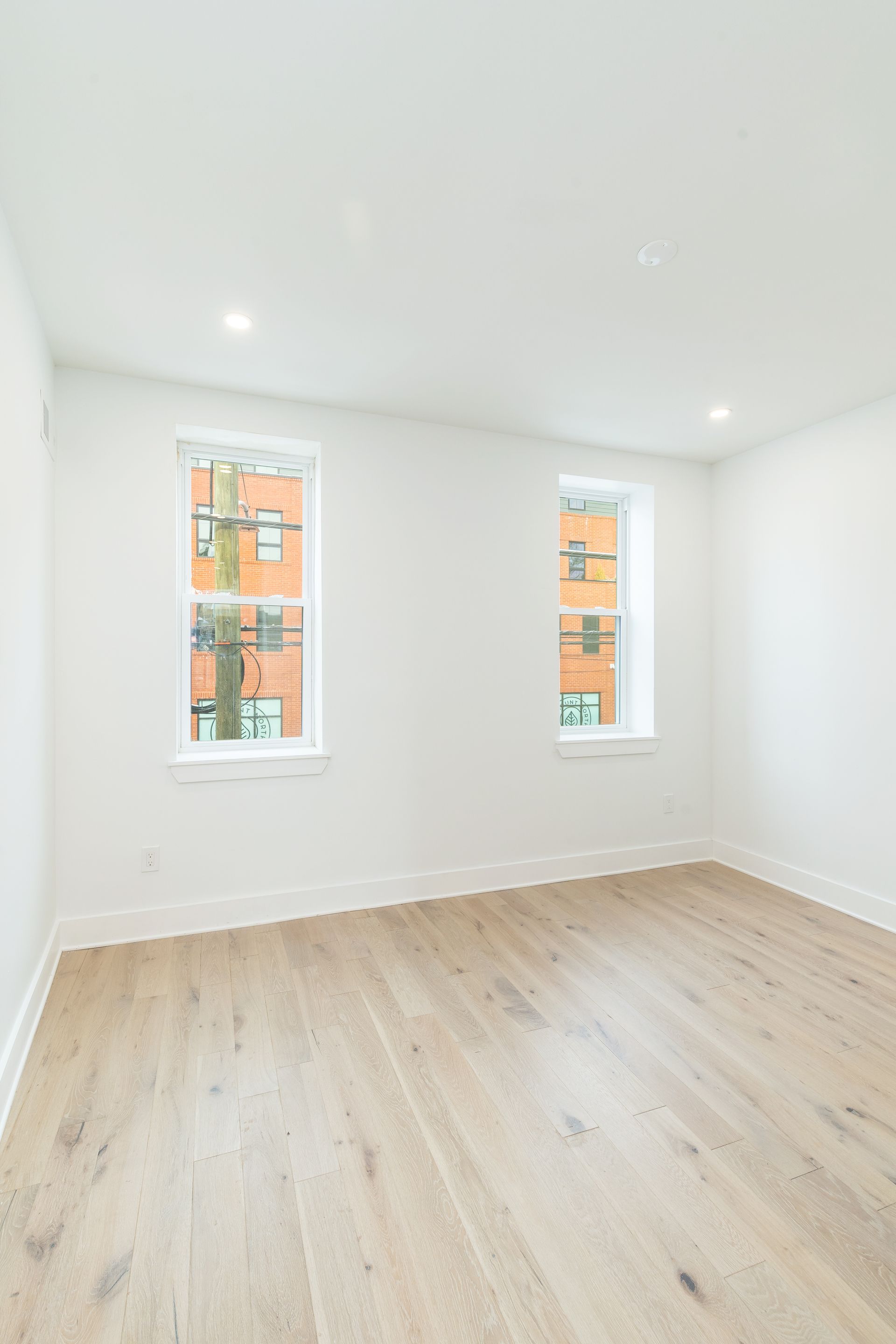 An empty room with hardwood floors and two windows.