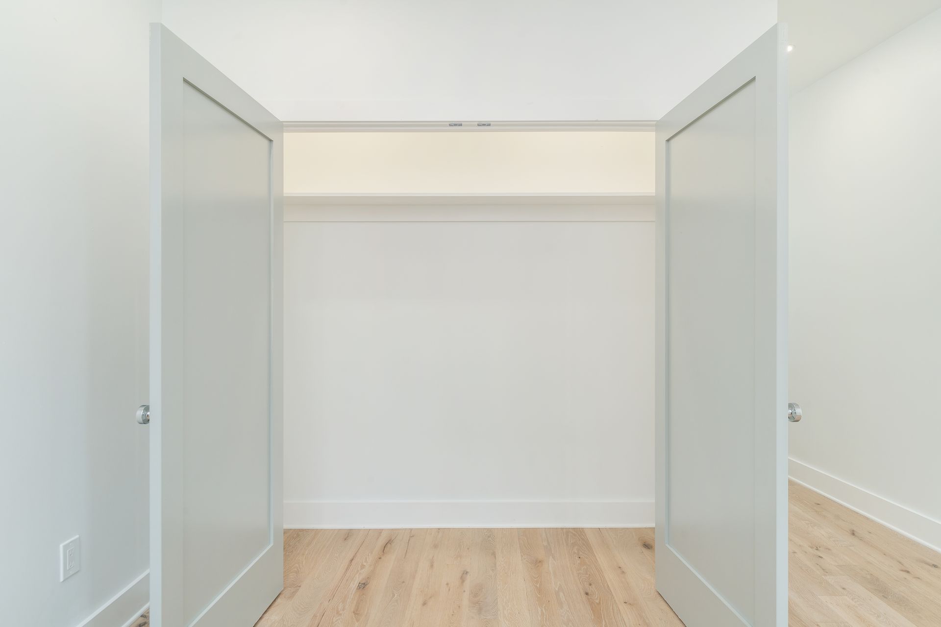 An empty closet with white doors and wooden floors.