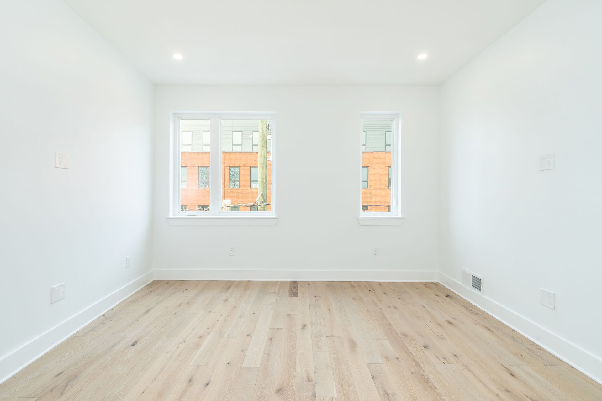 An empty room with hardwood floors and two windows.