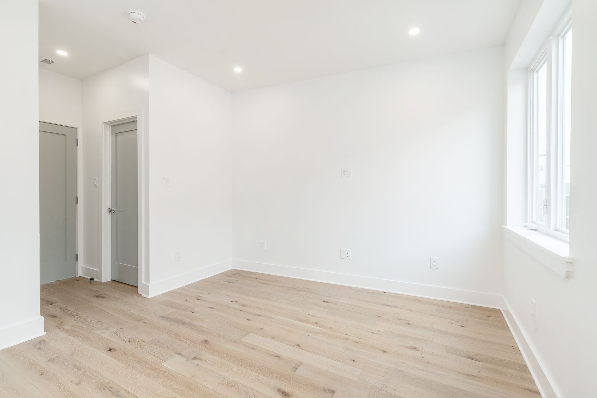 An empty bedroom with hardwood floors and white walls.