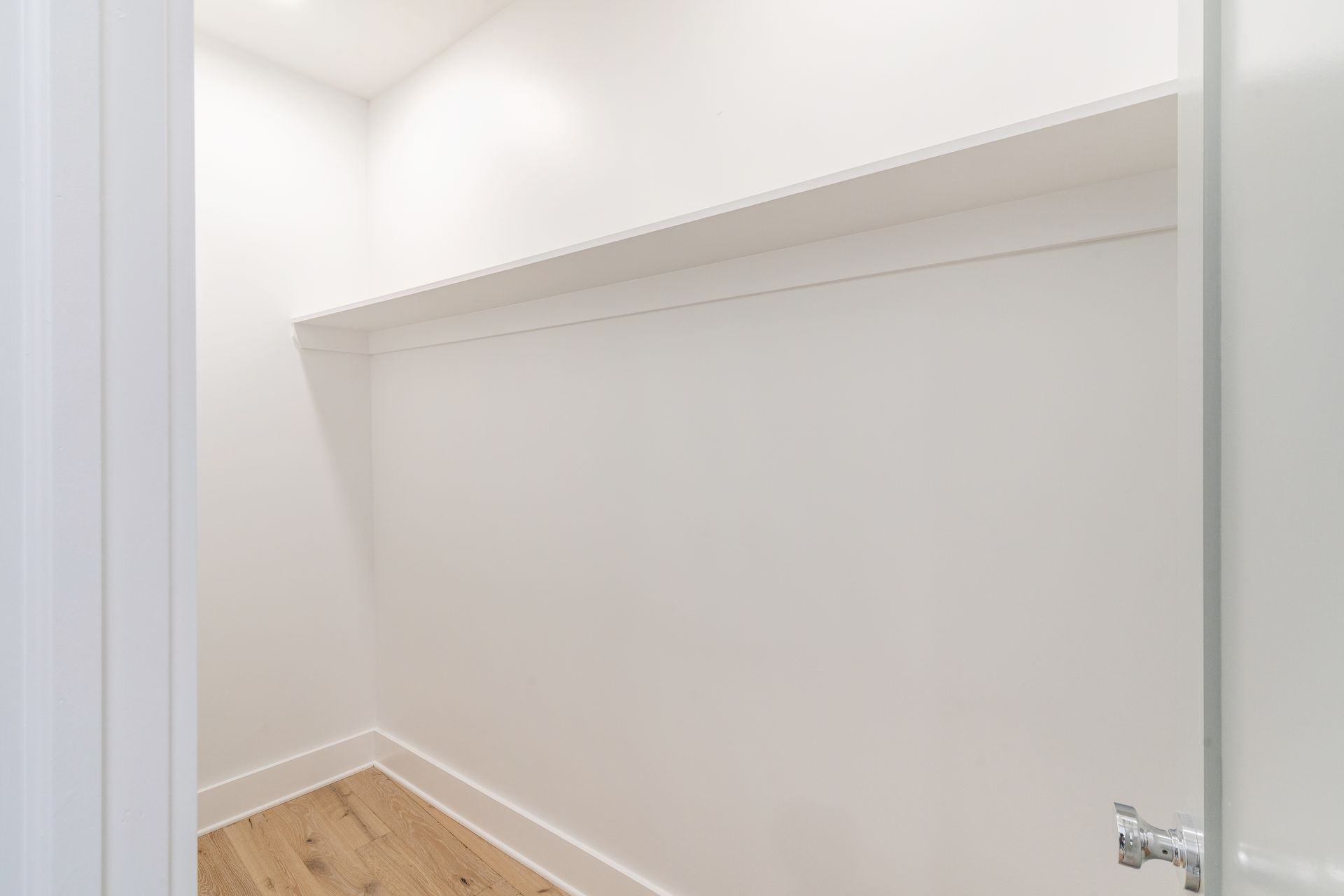 An empty walk in closet with a wooden floor and white walls.